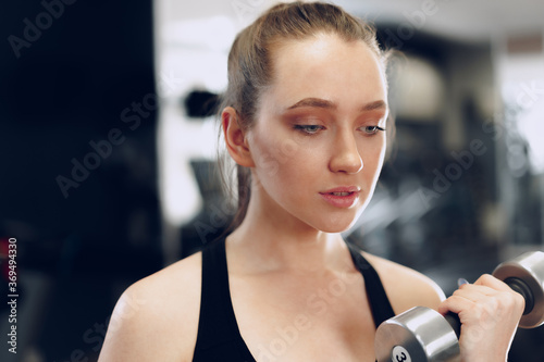 Young brunette sporty woman exercising with dumbbell in a gym