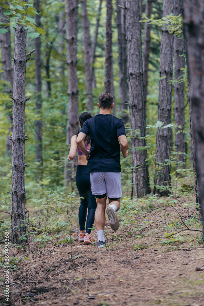 Young athletic couple is running outdoors in the wooded forest area Young athletic couple is running outdoors in the wooded forest area
