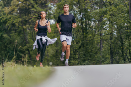 Fototapeta Naklejka Na Ścianę i Meble -  Young fit couple atheltes running on running road in a forest.