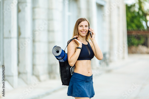 Young athletic woman with water phone and sports mat doing sport outside in bright sports suit photo