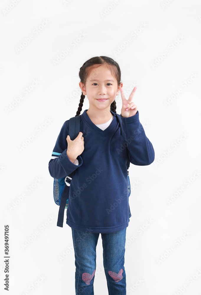 Cute asian little child girl in casual school uniform with backpack showing finger fight or victory sign on white background. Studio shot Cute asian little child girl in casual school uniform with backpack showing finger fight or victory sign on white background. Studio shot