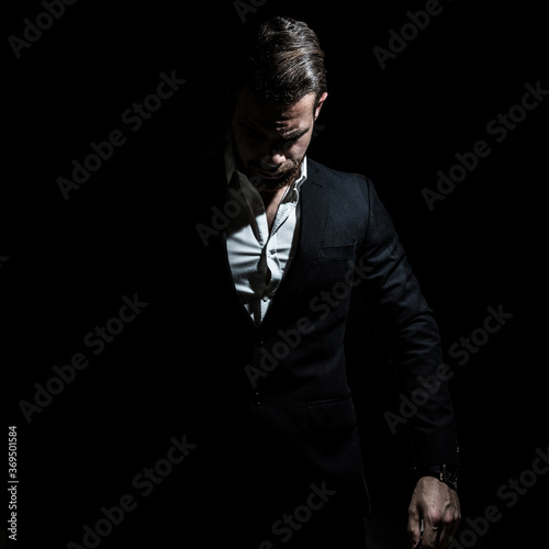 Business portrait of a young caucasian man in a black classic suit on a black background. 