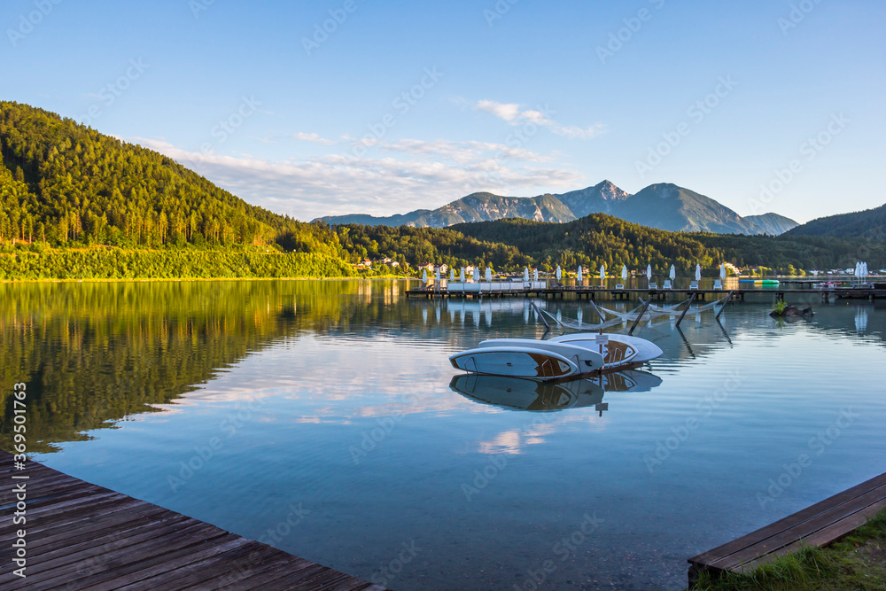 A view of a mountain alpine lake on a evening. Lake with hills, water and blue sky with clouds. Green forest by the lake in reflection in the water beauty in nature A view of a mountain alpine lake on a evening. Lake with hills, water and blue sky with clouds. Green forest by the lake in reflection in the water beauty in nature