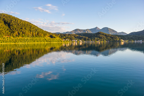 A view of a mountain alpine lake on a evening. Lake with hills, water and blue sky with clouds. Green forest by the lake in reflection in the water beauty in nature © Anna 