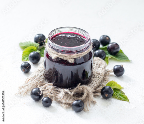 Black currant jam in a jar on a light background in rustic style