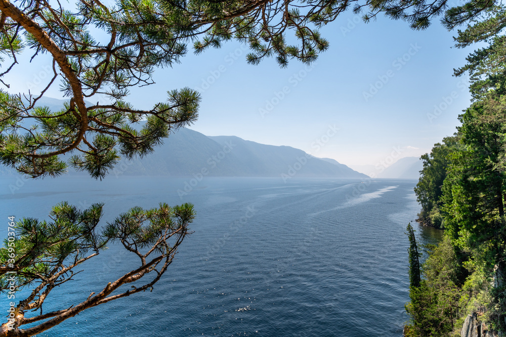 Obraz premium the boat goes along the mountain lake. beautiful lake in the mountains. cedar branches hang over the lake