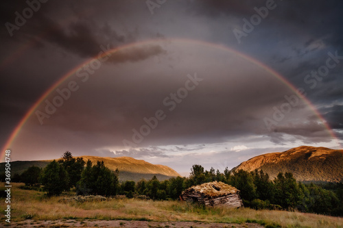Scenic view of rainbow over mountains with hut in foreground
