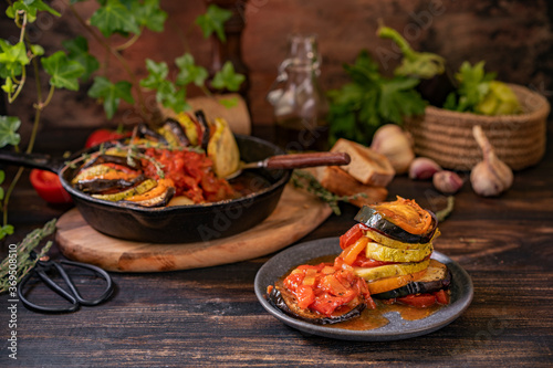 Ratatouille made of zucchini, eggplants, peppers, onions, garlic and tomatoes slices with aromatic herbs, bread. Rustic wooden table. Traditional French food, vegetable, vegan healthy dish. Copy space