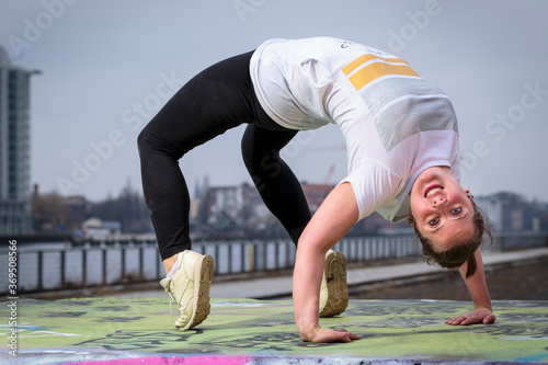 Young active and energetic woman in an urban context makes an inverted arch during a street dance workout session. Horizontal close-up portrait photo