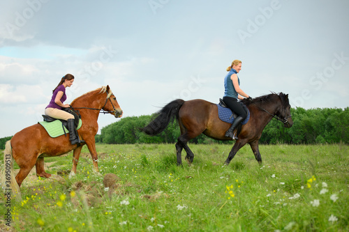 Two Caucasian horsewomen are overcoming the slope in rural.