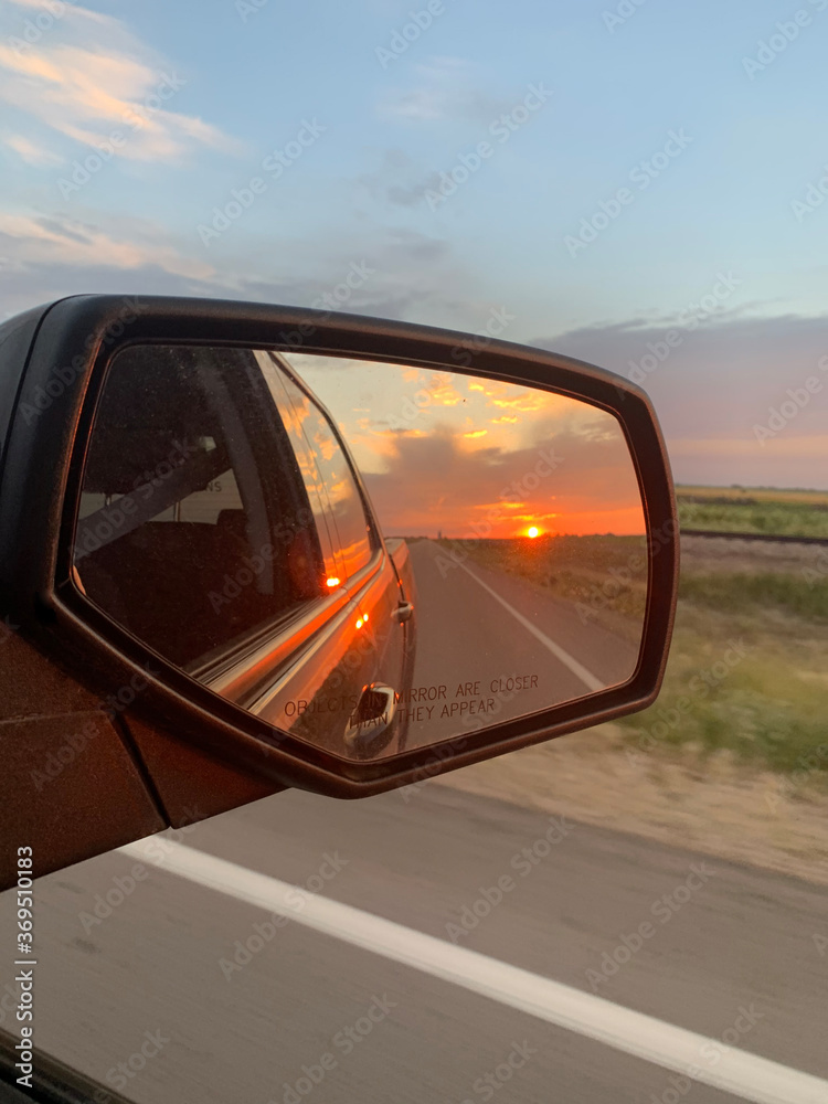 Car driving on road with sunset in mirror