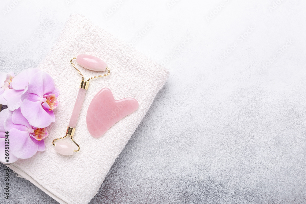Rose Quartz jade roller and Gua Sha massager on towel on stone background. Massage tool for facial skin care, SPA beauty treatment concept Rose Quartz jade roller and Gua Sha massager on towel on stone background. Massage tool for facial skin care, SPA beauty treatment concept