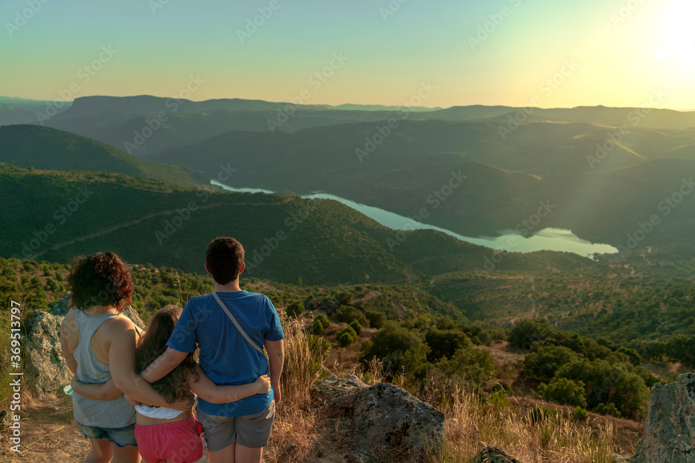 Fototapeta premium A woman with her children, a boy and a girl, watching from the top of the valley the mountains and the Douro River as the sun sets at dusk. Vilvestre, Spain