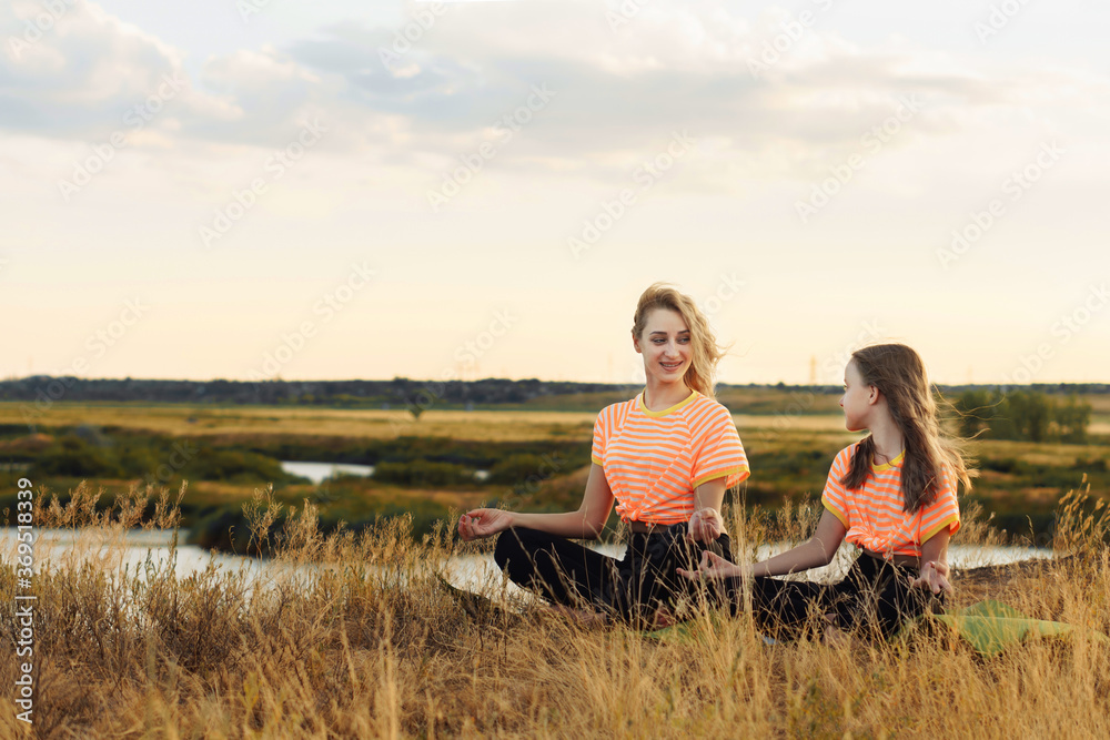 Young mother with her daughter in same clothes making yoga outdoors.