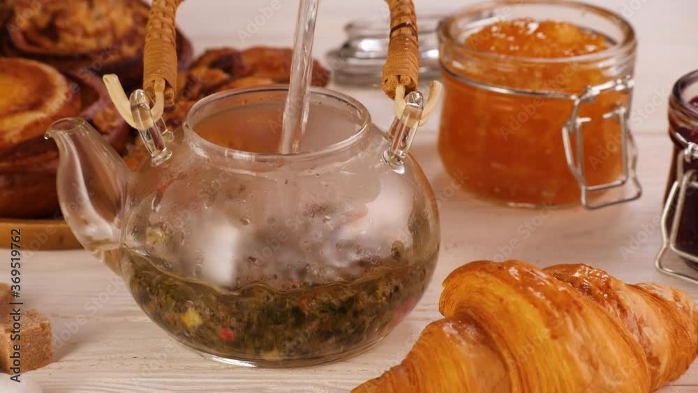High angle of unrecognizable person pouring water into teapot with fruit tea and putting lid on near assorted desserts on table during breakfast High angle of unrecognizable person pouring water into teapot with fruit tea and putting lid on near assorted desserts on table during breakfast