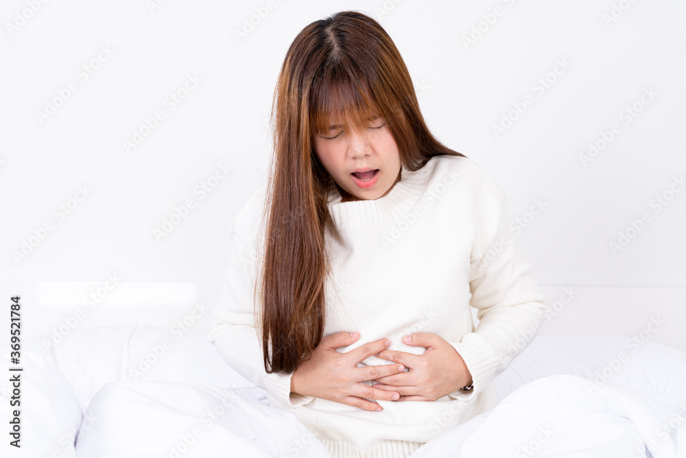 Young woman suffering stomach aches lying on the bed. Healthcare medical or daily life concept.