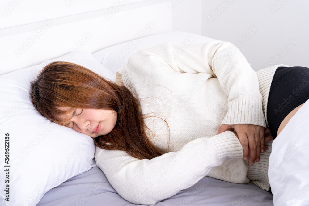 Young woman suffering stomach aches lying on the bed. Healthcare medical or daily life concept. Young woman suffering stomach aches lying on the bed. Healthcare medical or daily life concept.