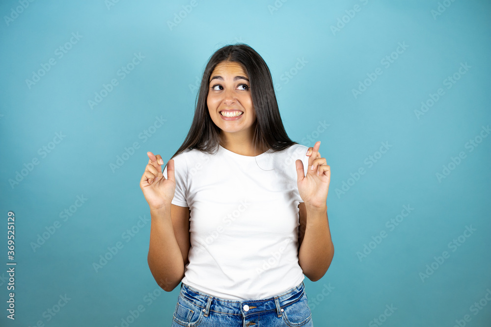 Fototapeta premium Young beautiful woman over isolated blue background gesturing finger crossed smiling with hope and looking side