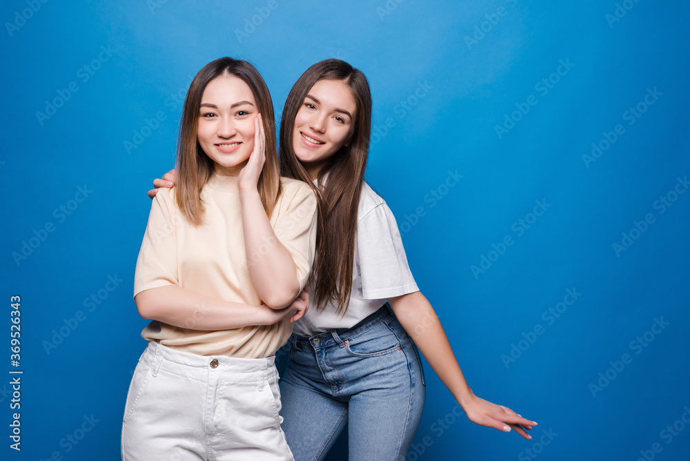 Portrait of two cheerful young women standing together and pointing finger isolated over blue background Portrait of two cheerful young women standing together and pointing finger isolated over blue background
