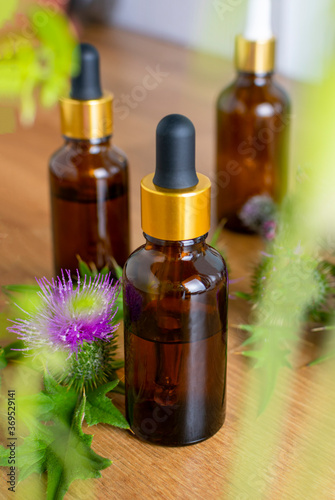 Cosmetic glass brown bottles with pipette and a flowers of burdock wooden background. In the foreground  the greenery is out of focus. Saturated colors.