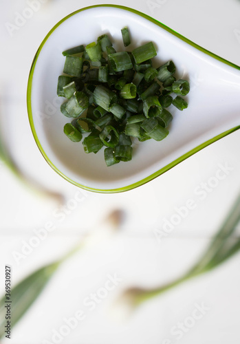 Chopped fresh green onions in spoon  on blurred background of whole onions. Top view.