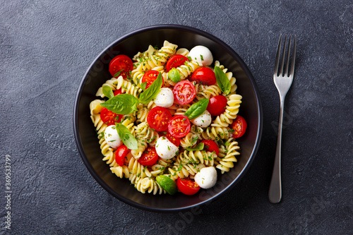 Pasta fusilli with mozzarella cheese, tomatoes and basil. Dark background. Close up. Top view.