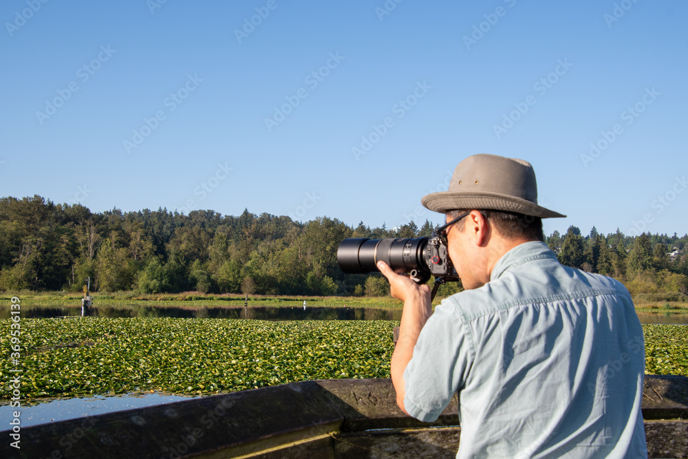 望遠レンズ付けた一眼レフカメラでネイチャ－フォト撮影をするサングラスをかけたアジア人男性　　バンクーバー　ブリティッシュコロンビア　カナダ
