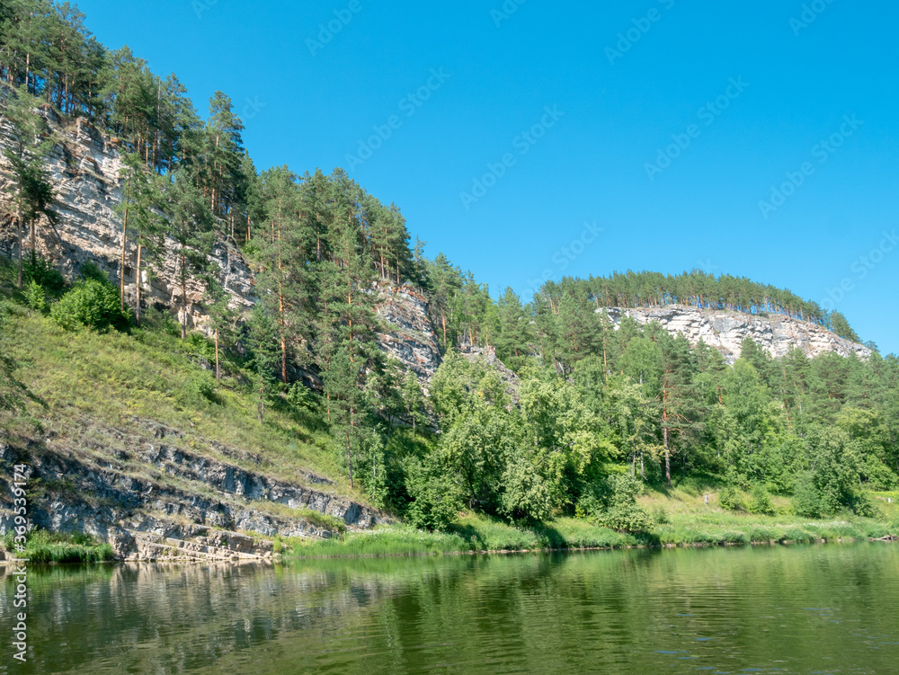 Landscape, river, mountains, forests on a summer day. Rocky shore with the forest.