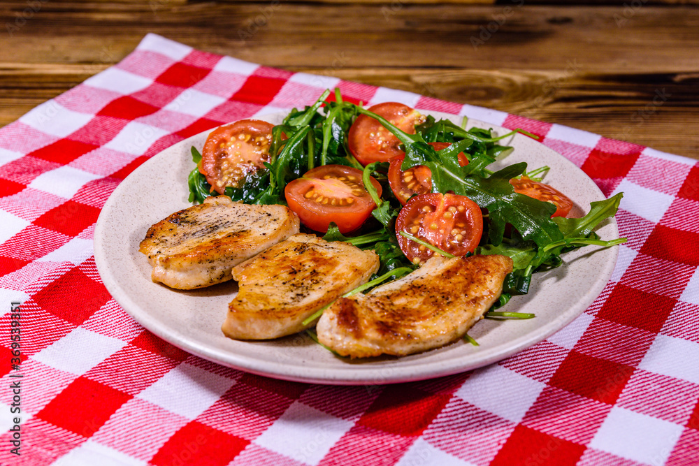 Roasted chicken breasts and salad with arugula and cherry tomatoes in a ceramic plate
