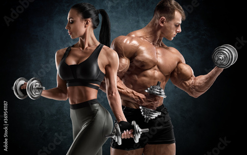 Sporty couple workout with dumbbells. Muscular man and woman showing muscles