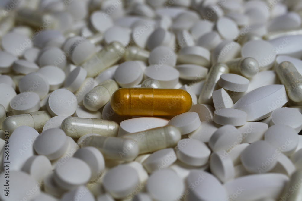 Full frame closeup of pile countless white pills and capsules with one yellow capsule in center (focus on yellow pill) Full frame closeup of pile countless white pills and capsules with one yellow capsule in center (focus on yellow pill)