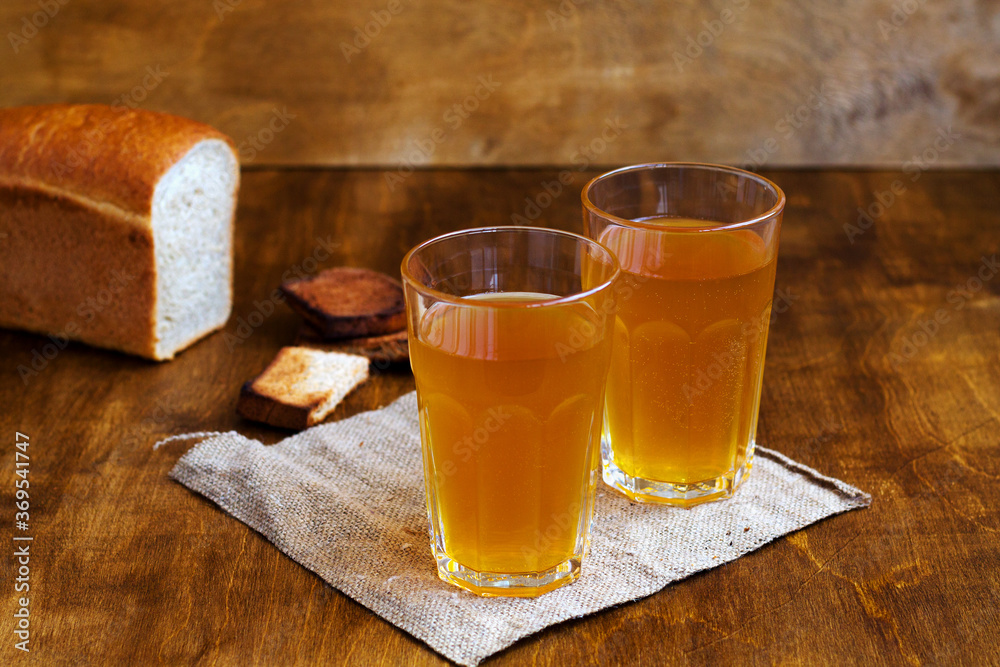 Cold drink. Two glasses of homemade bread kvass with black rye bread and hard chucks on a wooden table. Beer with sackcloth on brown background. summer soft drink. Cold drink. Two glasses of homemade bread kvass with black rye bread and hard chucks on a wooden table. Beer with sackcloth on brown background. summer soft drink.