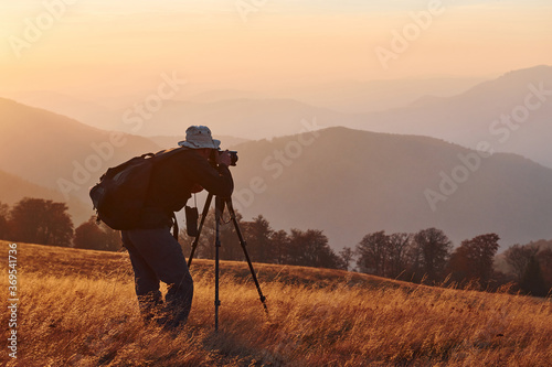 Male photographer standing and working at majestic landscape of autumn trees and mountains by the horizon