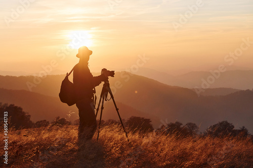 Male photographer standing and working at majestic landscape of autumn trees and mountains by the horizon
