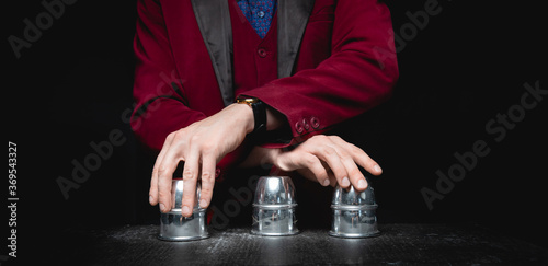 Magician shows shell game of thimbles with circles and ball, black background. Concept deception, sleight hand