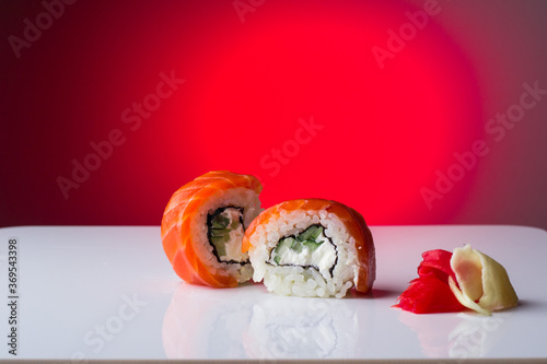 Two fresh and juicy sushi with red fish salmon, cream cheese, ginger, cucumber, avacado, with reflection, on a ruck white background