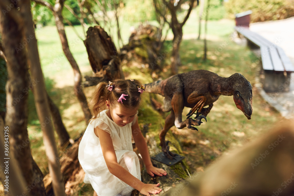 Cheerful little girl having fun in park with dinosaur replicas outdoors