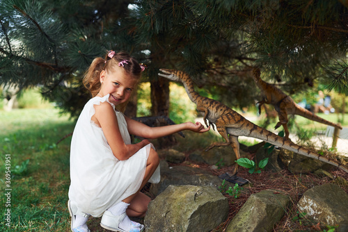 Cheerful little girl having fun in park with dinosaur replicas outdoors photo