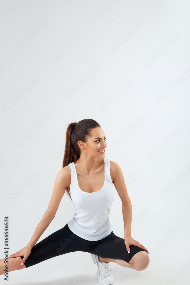 Pretty joyful young sportswoman in tracksuit standing and warming up isolated over grey background