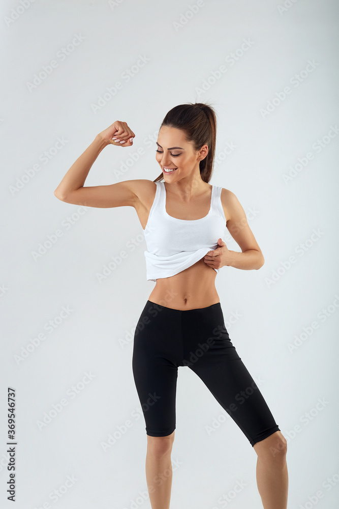 Attractive young adult in sportswear posing on grey background. Sexy and sensual brunette woman with perfect body posing in studio isolated over grey background with copyspace. Attractive young adult in sportswear posing on grey background. Sexy and sensual brunette woman with perfect body posing in studio isolated over grey background with copyspace.