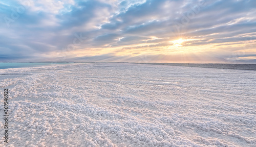 Fototapeta Naklejka Na Ścianę i Meble -  Crystalline white salt beach lit by morning sun, small puddles with seawater at Dead Sea - world most hypersaline lake