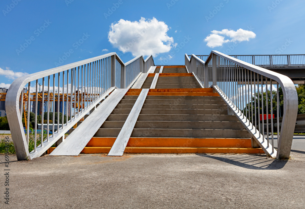 Pedestrian crossing stairs over the highway against the background of the blue sky and white clouds.