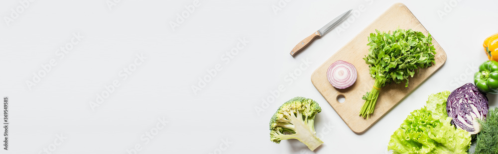 top view of ripe vegetables near wooden cutting board with parsley and onion on white surface, panoramic shot