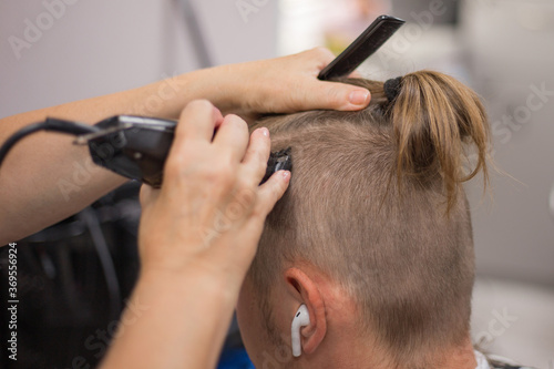 Barber's hands cut hair with hair clipper and comb. A male gets a trendy haircut. Barber services.