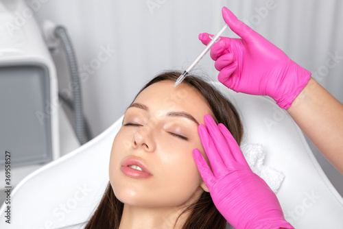 Cosmetologist makes rejuvenating anti wrinkle injections on the chin, cheeks and neck of a beautiful brunette woman. Female aesthetic cosmetology in a beauty salon.