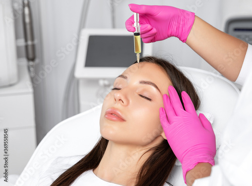 The beautician makes an anti-wrinkle PRP injections on the face to a beautiful woman at the beautician. Female aesthetic cosmetology in a beauty salon.