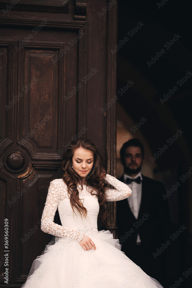 Beautiful newlyweds near the ancient door. Wedding portrait of a stylish groom and a young bride near old house in in a European town