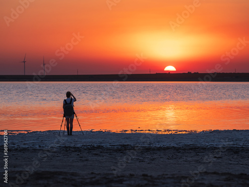 silhouette of girl photographer who shooting landscape with sunset and water