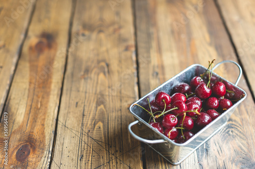 Fresh red ripe organic macro sweet cherry with waterd drops in metal basket on wooden background. space for text. closeup photo