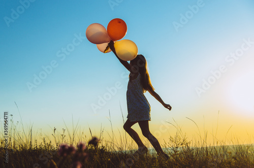 Silhouette of a child walking with balloons on a hill backlit by sunset golden light, concept of freedom and carelessness 